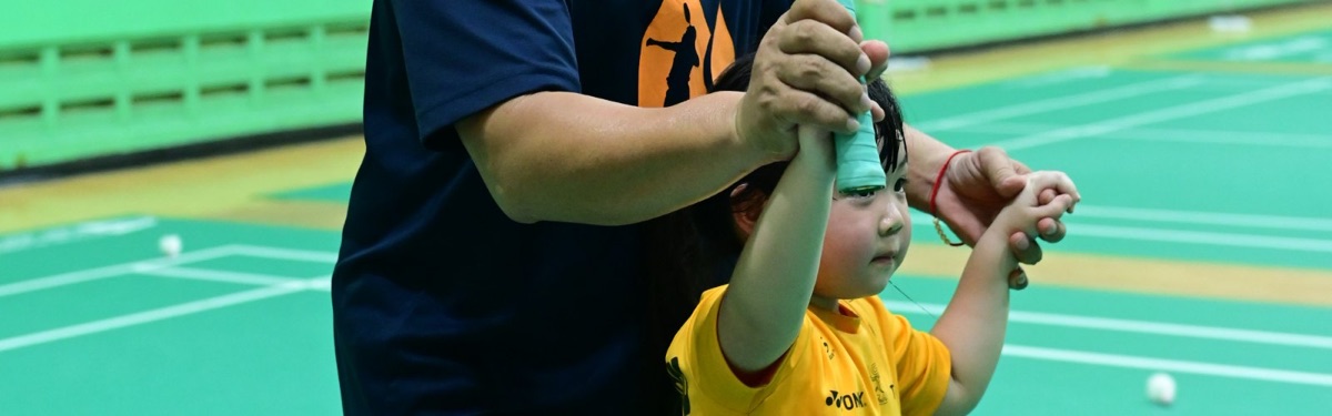 โค้ชจับมือนักเรียนตัวเล็กสอนจับไม้แบดมินตันแบบตัวต่อตัว