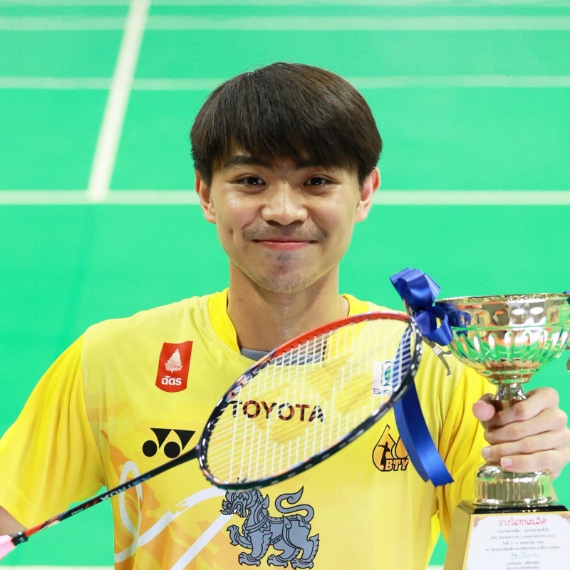 คิมหันต์ ธนวัฒน์ ยิ้มจิตต์ ถือไม้แบดและถ้วยรางวัลชนะเลิศในสนามแข่ง