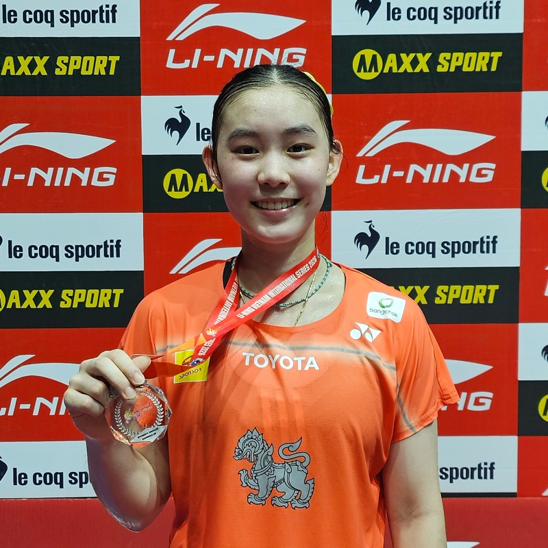 Sarunrak “Som” Vitidsarn, a Banthongyord player, holding her medal in front of the tournament board
